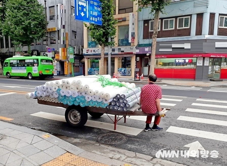 ▲ 서울지하철 1호선 종로5가역 사거리에서 한 70대 노인이 배달용 수레에 옷감 두루마리를 실고, 횡단보도를 건너기 전에 다리쉼을 하고 있다. (사진=내외방송 정수남 기자)