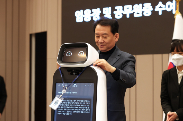 지난 13일 시연회를 마친 뒤 국회 1호 AI로봇 '큐아이'에게 이광재 국회사무총장이 공무원증을 걸어주고 있다.(사진=국회사무처)